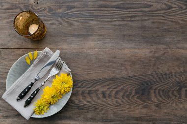 Rustik sofra keten peçete, çatal bıçak takımları, seramik kaplamalar, sarı gözlük ve koyu ahşap masaya sarı çiçek. Tatil masa dekorasyonu. Romantik bir akşam yemeği.