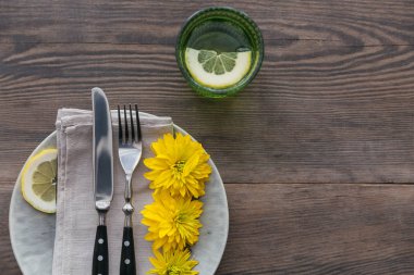 Rustik sofra keten peçete, çatal bıçak takımları, seramik kaplamalar, sarı gözlük ve koyu ahşap masaya sarı çiçek. Tatil masa dekorasyonu. Romantik bir akşam yemeği.