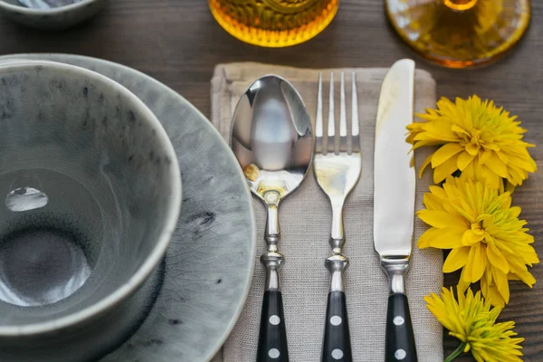 Rustik sofra keten peçete, çatal bıçak takımları, seramik kaplamalar, sarı gözlük ve koyu ahşap masaya sarı çiçek. Tatil masa dekorasyonu. Romantik bir akşam yemeği.