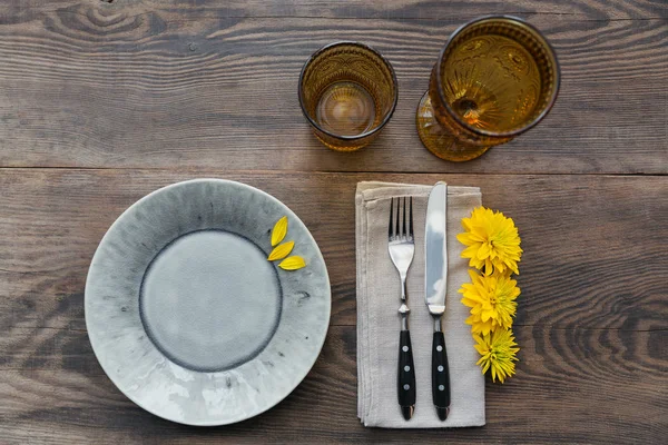 Rustik sofra keten peçete, çatal bıçak takımları, seramik kaplamalar, sarı gözlük ve koyu ahşap masaya sarı çiçek. Tatil masa dekorasyonu. Romantik bir akşam yemeği.