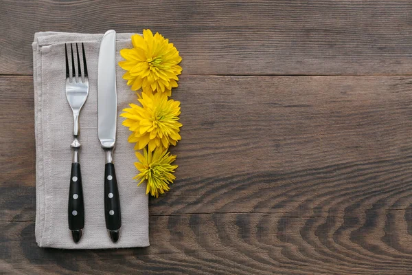 Rustic table setting with linen napkin, cutlery, ceramic plates, yellow glasses and yellow flowers on dark wooden table. Holiday table decoration. Romantic dinner.