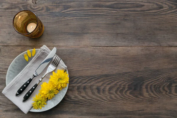 Rustik sofra keten peçete, çatal bıçak takımları, seramik kaplamalar, sarı gözlük ve koyu ahşap masaya sarı çiçek. Tatil masa dekorasyonu. Romantik bir akşam yemeği.