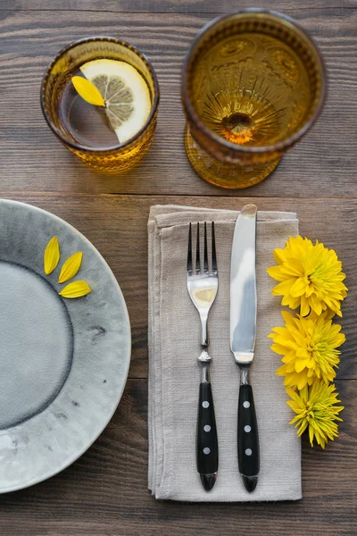 Rustik sofra keten peçete, çatal bıçak takımları, seramik kaplamalar, sarı gözlük ve koyu ahşap masaya sarı çiçek. Tatil masa dekorasyonu. Romantik bir akşam yemeği.