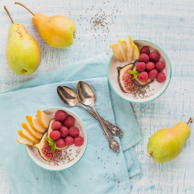 Taze meyve, chia tohum, ahududu ve sağlıklı vegan vejetaryen diyet kahvaltı için beyaz rustik ahşap arka plan üzerinde incir ile güler yüzlü kase. Sağlıklı gıda kavramı. Düz yatıyordu