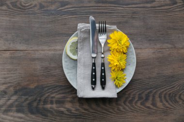 Rustik sofra keten peçete, çatal bıçak takımları, seramik kaplamalar, sarı gözlük ve koyu ahşap masaya sarı çiçek. Tatil masa dekorasyonu. Romantik bir akşam yemeği.