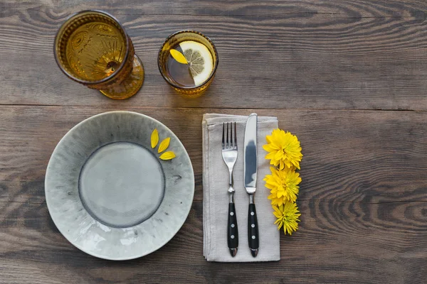 Rustik sofra keten peçete, çatal bıçak takımları, seramik kaplamalar, sarı gözlük ve koyu ahşap masaya sarı çiçek. Tatil masa dekorasyonu. Romantik bir akşam yemeği.