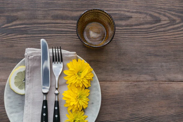 Rustik sofra keten peçete, çatal bıçak takımları, seramik kaplamalar, sarı gözlük ve koyu ahşap masaya sarı çiçek. Tatil masa dekorasyonu. Romantik bir akşam yemeği.