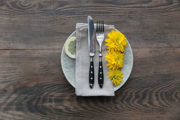 Rustik sofra keten peçete, çatal bıçak takımları, seramik kaplamalar, sarı gözlük ve koyu ahşap masaya sarı çiçek. Tatil masa dekorasyonu. Romantik bir akşam yemeği.