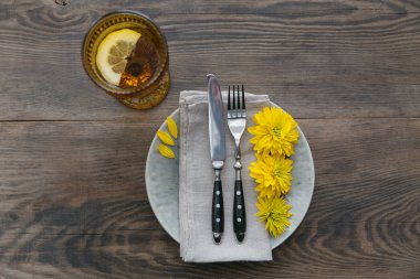 Rustik sofra keten peçete, çatal bıçak takımları, seramik kaplamalar, sarı gözlük ve koyu ahşap masaya sarı çiçek. Tatil masa dekorasyonu. Romantik bir akşam yemeği.