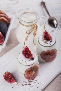 İncir ve rustik beyaz zemin üzerine chia tohum ile sağlıklı ev yapımı yoğurt cam kavanozlar. Süt ve süt ürünleri. Sağlıklı gıda, diyet ve kahvaltı konsepti. Taze yoğurt tohum ve meyve ile yapılmış.