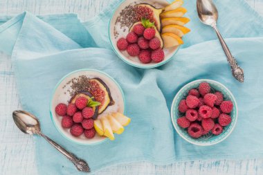 Taze meyve, chia tohum, ahududu ve sağlıklı vegan vejetaryen diyet kahvaltı için beyaz rustik ahşap arka plan üzerinde incir ile güler yüzlü kase. Sağlıklı gıda kavramı. Üstten görünüm