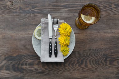 Rustik sofra keten peçete, çatal bıçak takımları, seramik kaplamalar, sarı gözlük ve koyu ahşap masaya sarı çiçek. Tatil masa dekorasyonu. Romantik bir akşam yemeği.