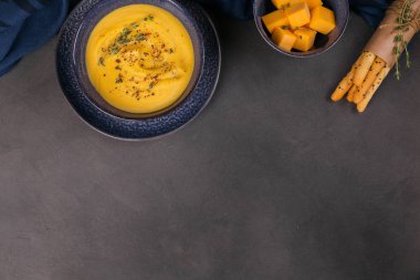 Koyu arka plan üzerinde taze ot ile tepesinde mavi kapta balkabağı çorbası. Sağlıklı sebze gıda diyet için.