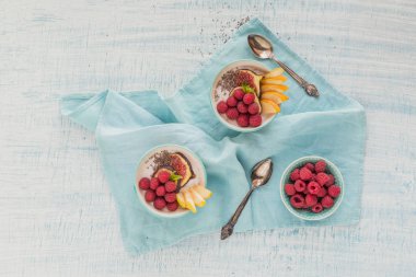 Taze meyve, chia tohum, ahududu ve sağlıklı vegan vejetaryen diyet kahvaltı için beyaz rustik ahşap arka plan üzerinde incir ile güler yüzlü kase. Sağlıklı gıda kavramı. Düz yatıyordu