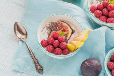 Taze meyve, chia tohum, ahududu ve sağlıklı vegan vejetaryen diyet kahvaltı için beyaz rustik ahşap arka plan üzerinde incir ile güler yüzlü kase. Sağlıklı gıda kavramı. 
