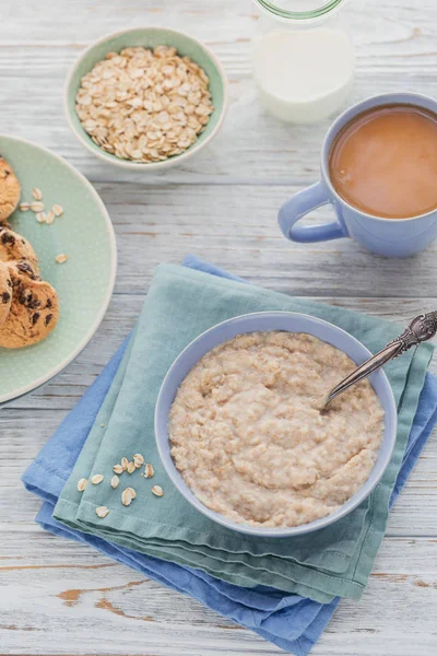 Oatmeal porridge bowl and tea with milk on the white wooden background. Healthy nutritious breakfast. Concept of healthy eating, dieting.