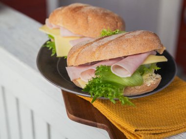 Jambon, peynir ve marul rustik ahşap zemin üzerine iki taze ciabatta baget sandviçler. Açık piknik yaşam tarzı.