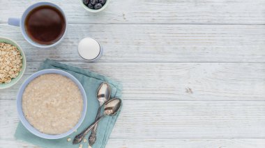 Oatmeal porridge bowl with berry and black tea on the white wooden background. Healthy nutritious breakfast. Concept of healthy eating, dieting. Top view with free space for text clipart
