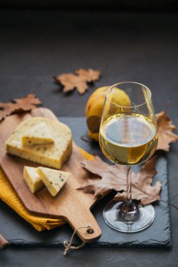 Bir kadeh beyaz şarap bir kesme tahtası koyu arka plan üzerinde beyaz peynir ile görev almıştı. Peynir, şarap ve rustik tarzda kuru yaprakları ile sonbahar piknik.