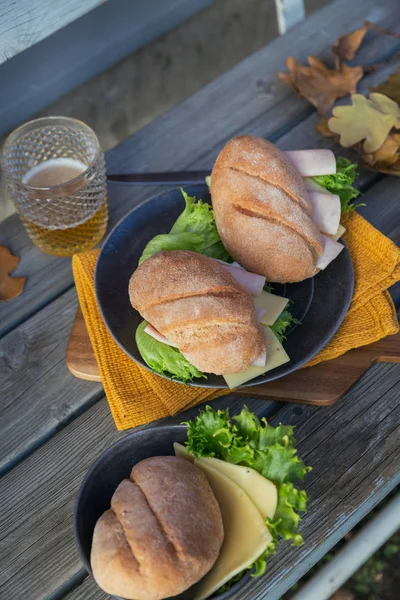 两个新鲜的跟面包三明治 包括火腿 生菜和一杯啤酒 以质朴的木制为背景 户外秋季野餐生活方式 — 图库照片