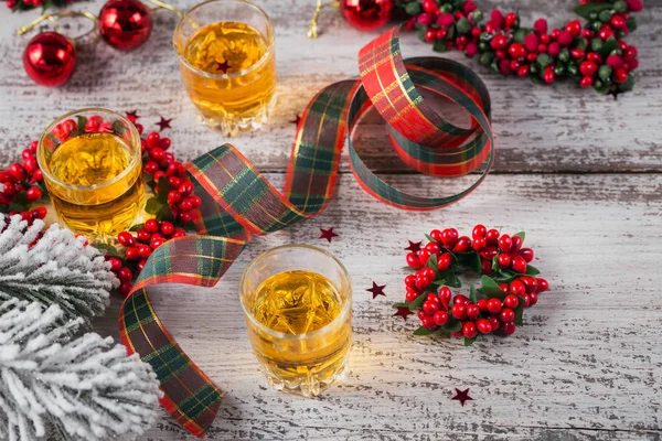 Whiskey, brandy or liquor shot and Christmas decorations on white wooden background. Seasonal holidays concept.