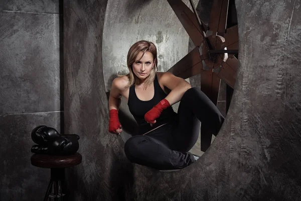 Sporting blonde woman in boxing bandages and boxing gloves around in dark studio looking at camera. Strong woman concept.