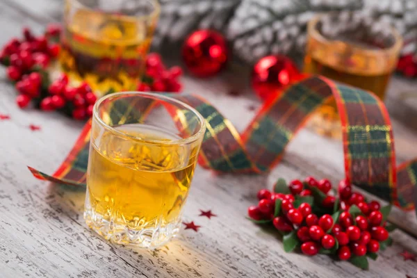 Whiskey, brandy or liquor shot and Christmas decorations on white wooden background. Seasonal holidays concept.