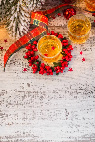 Whiskey, brandy or liquor shot and Christmas decorations on white wooden background. Winter holidays concept. Above
