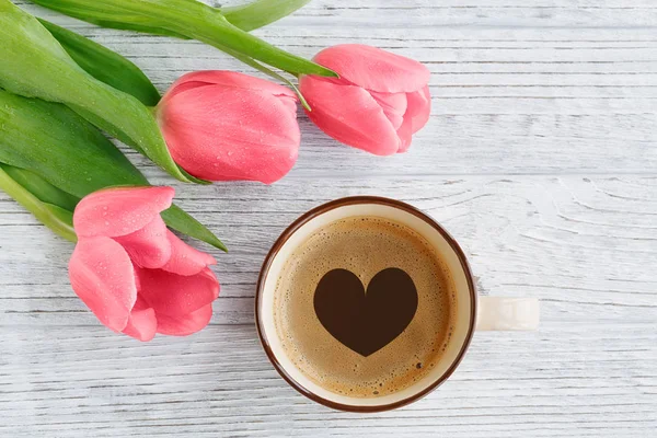 Coral tulips and coffee with heart shape on white rustic wooden background