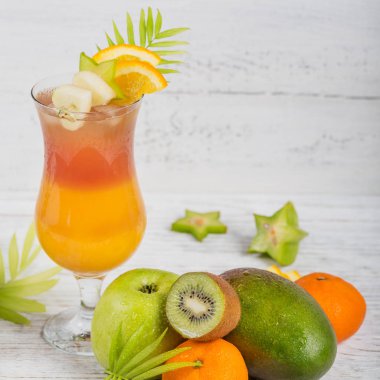Yaz ile çeşitli tropikal meyve kokteyl. Elma, kivi, mandalina, portakal, mango, carambola. Beyaz ahşap zemin üzerine portakal suyu bir bardak.