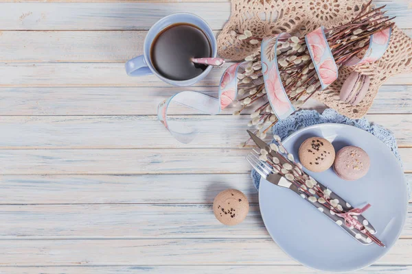 Easter table setting with coffee, macaroon cookies, willow branches and cutlery. Spring holiday concept