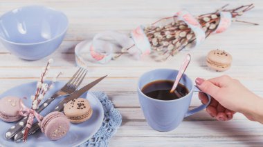 Paskalya sofra söğüt dalları, macaroons ve çatal bıçak takımı. Kadın el bir fincan kahve tutar. Bahar tatil kavramı