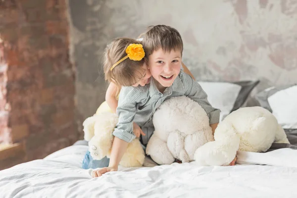 Hermano y hermana jugando con el oso de peluche en la cama — Foto de Stock