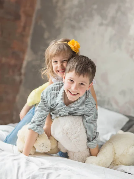 Hermano y hermana jugando con el oso de peluche en la cama — Foto de Stock