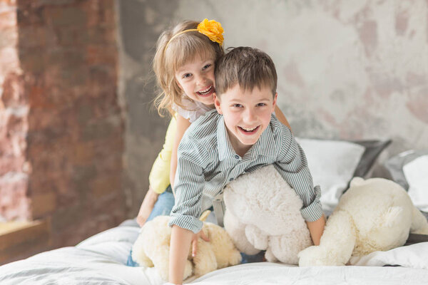 Brother and sister playing with teddy bear in bed