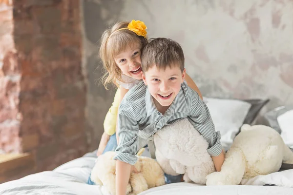 Hermano y hermana jugando con el oso de peluche en la cama — Foto de Stock