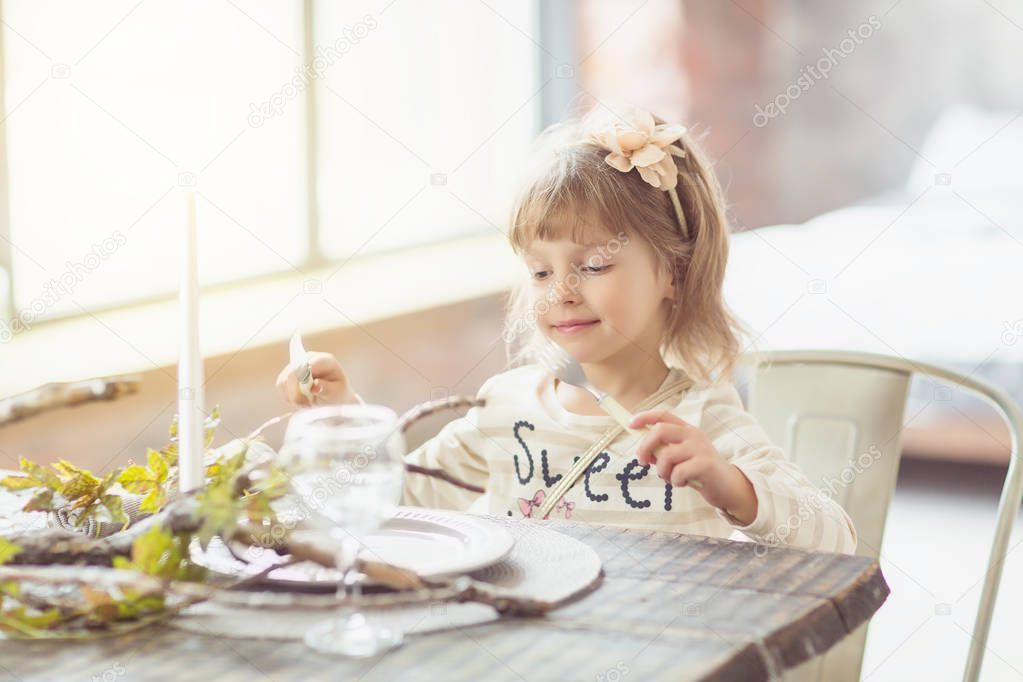 girl sitting at the table and holding fork and knife in her hand