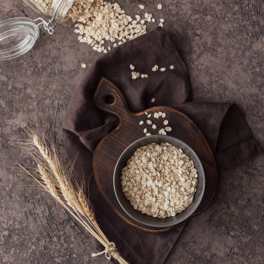 Koyu arkaplanda buğday kulaklı bir kase kuru yulaf lapası. Birlikte