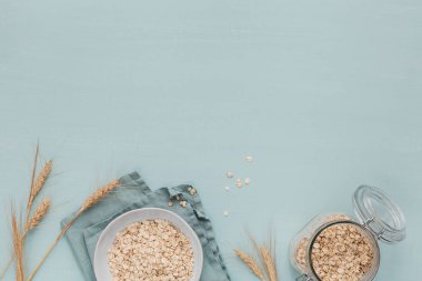 Bir kase kuru yulaf gevreği ve hafif arka planda buğday kulakları. C