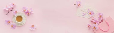 Sabah kahvesi, süt ya da kapuçino, mektup, pembe hediye paketi ve açık pembe arka planda mor orkide çiçekleri ile narin düz bir kompozisyon. Güzel kahvaltı konsepti. Uzun pankart