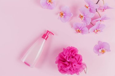 Kozmetik sabun, şampuan ya da duş jeli, pembe sünger ve açık pembe arkaplanda mor orkide çiçekleri olan plastik şeker kutusu. Spa ve sağlık konsepti