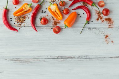 Beyaz ahşap masada çeşitli baharatlar, renkli biberler ve kiraz domatesleri. Metin için serbest baharat içeren baharatlar