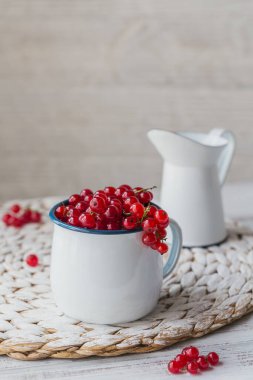 Beyaz mineli metal bir fincanda taze kırmızı frenk üzümü ve beyaz ahşap arka planda süt. Sağlıklı beslenme ve diyet gıda kavramı.