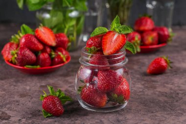 Kahverengi arka planda cam kavanozda taze çilek ve nane yaprağı yığını. Sağlıklı beslenme ve diyet gıda kavramı.