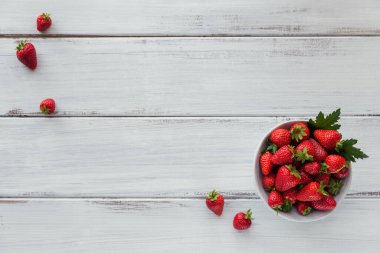Seramik kasede taze çilekler. Beyaz ahşap masadaki sağlıklı yiyecekler masal gibi. Lezzetli, tatlı, sulu ve olgun arkaplanlı metin için kopya alanı