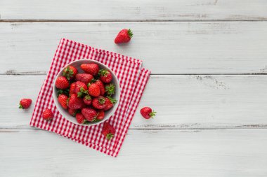 Seramik kasenin üstünde taze çilekler. Beyaz ahşap masa maketinde sağlıklı yiyecekler. Lezzetli, tatlı, sulu ve olgun arkaplanlı metin için kopya alanı
