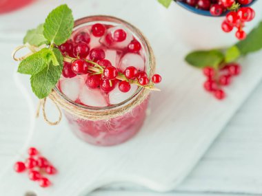 Beyaz köpüklü şaraplı yaz içkisi. Ev yapımı taze meyve kokteyli veya şampanyalı punç, kırmızı frenk üzümü, buz küpleri ve beyaz ahşap arka planda nane yaprakları.