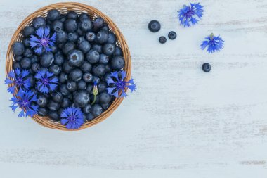 Çiçek desenli sepetli taze yaban mersini. Beyaz masadaki sağlıklı yiyecekler masal gibi. Lezzetli, tatlı, sulu ve olgun arkaplanlı metin için kopya alanı