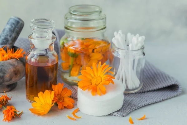 Natural cosmetic oil, tincture or infusion, cotton pad, sticks and towels with calendula flowers on light background. Healthy skin care. Aromatherapy, spa and wellness concept