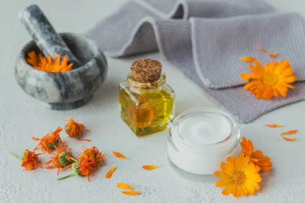 Natural cosmetic oil, tincture or infusion, ointment, cream or balm and mortar with calendula flowers dry and fresh on light background. Healthy skin care. Aromatherapy, spa and wellness concept